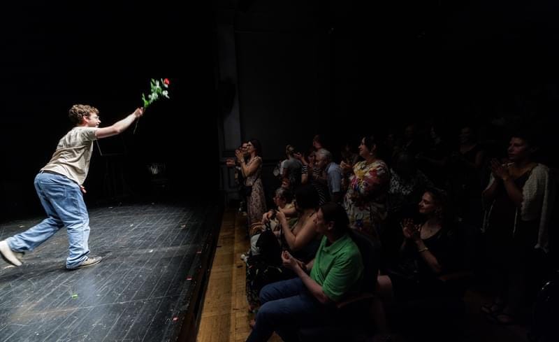 Jack stands on stage facing the audience. He holds a rose out to the audience, with his arm. The audience applaud him. Some people are standing in ovation.