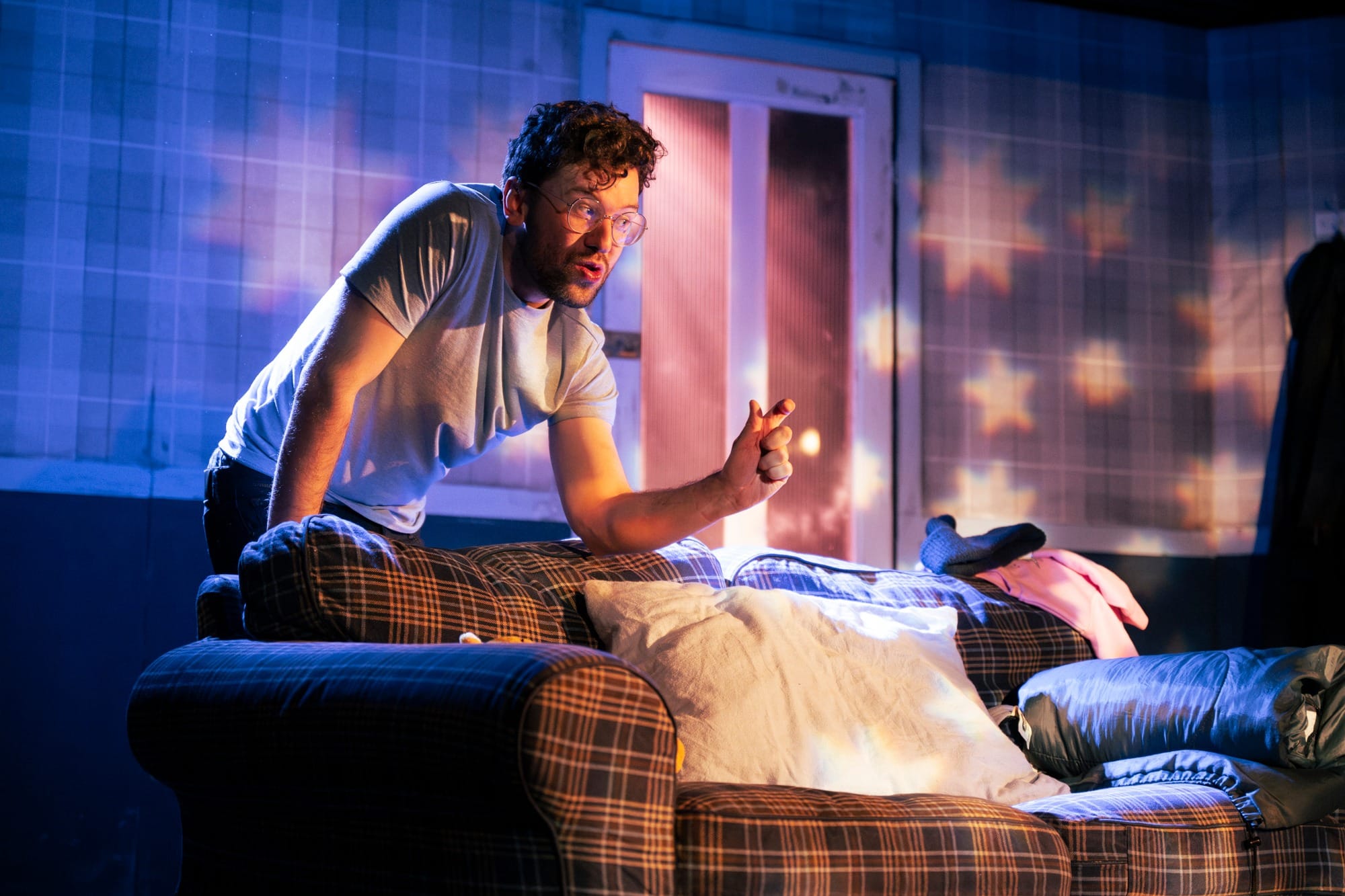 A man leans over the sofa in an excited manner. Stars from a child's mobile project onto the wall.