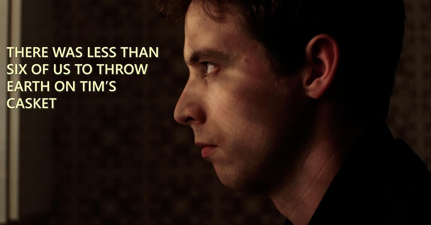 A man stands, in profile, in darkness, staring out a window. His face is mournful. Light from outside flickers on his face. Text: 